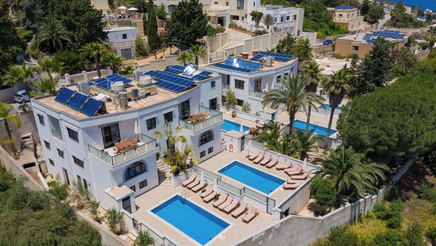 A modern villa with rooftop solar panels, two swimming pools, and a poolside lounge area.