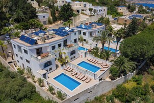 En modern villa med solpaneler på taket, två swimmingpooler och en loungeyta vid poolen.