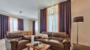 A spacious living room with two brown leather sofas, a wooden coffee table, and a dining area with a table and chairs.