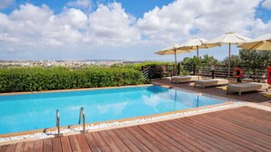 A rooftop pool with lounge chairs and umbrellas, surrounded by greenery and overlooking a cityscape. - Villa Munqar (Zurrieq)