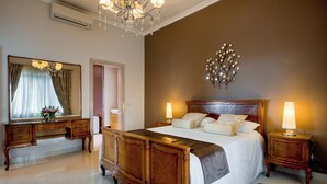 A bedroom with a large bed, wooden headboard, two bedside tables with lamps, a mirror, and a chandelier. - Villa Munqar (Zurrieq)