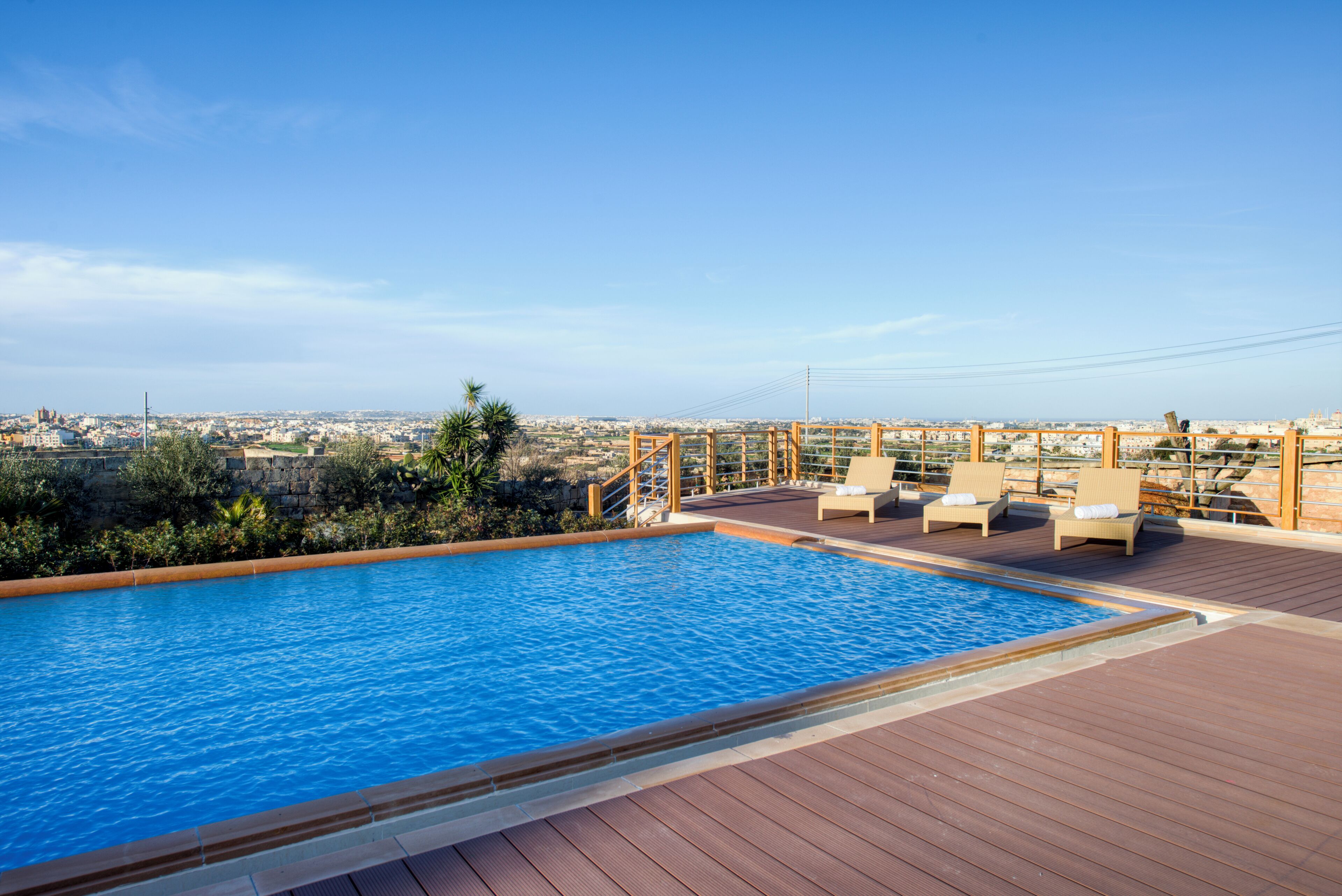 A rooftop pool with wooden deck, lounge chairs, and a view of the cityscape.