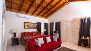 Ein Zimmer mit einem roten Sofa, einem Bild an der Wand, einer weißen Tür und einer Holzbalkendecke.