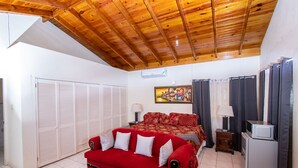 Ein Schlafzimmer mit Holzbalkendecke, einem roten Sofa, einem Bett mit gemustertem Überwurf, einem Fernseher auf einem kleinen Tisch und einem Kühlschrank.