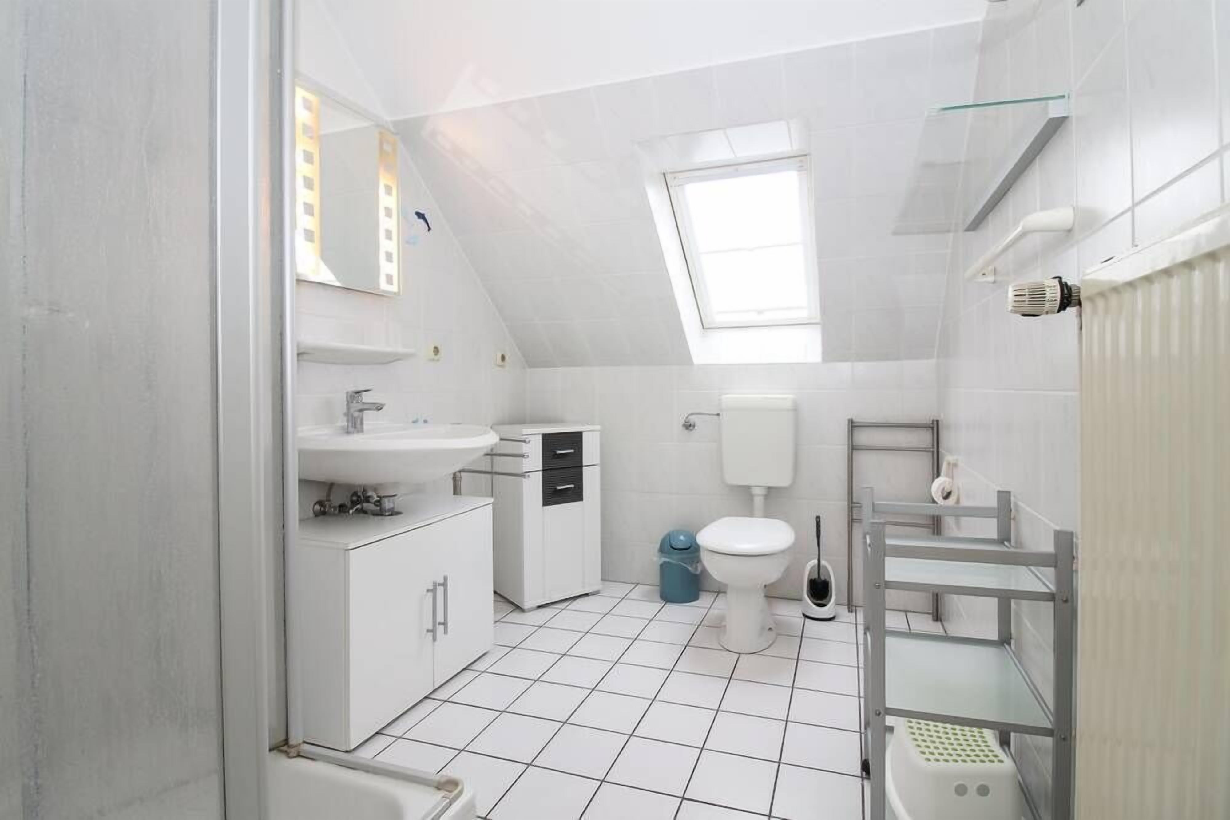 A compact, modern bathroom with a skylight, white fixtures, and a tiled floor.