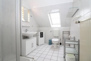 A compact, modern bathroom with a skylight, white fixtures, and a tiled floor. - Ferienhaus Ankerboje (Krummhoern)