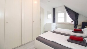 A bedroom with two beds, a wardrobe, a window with curtains, and a radiator.
