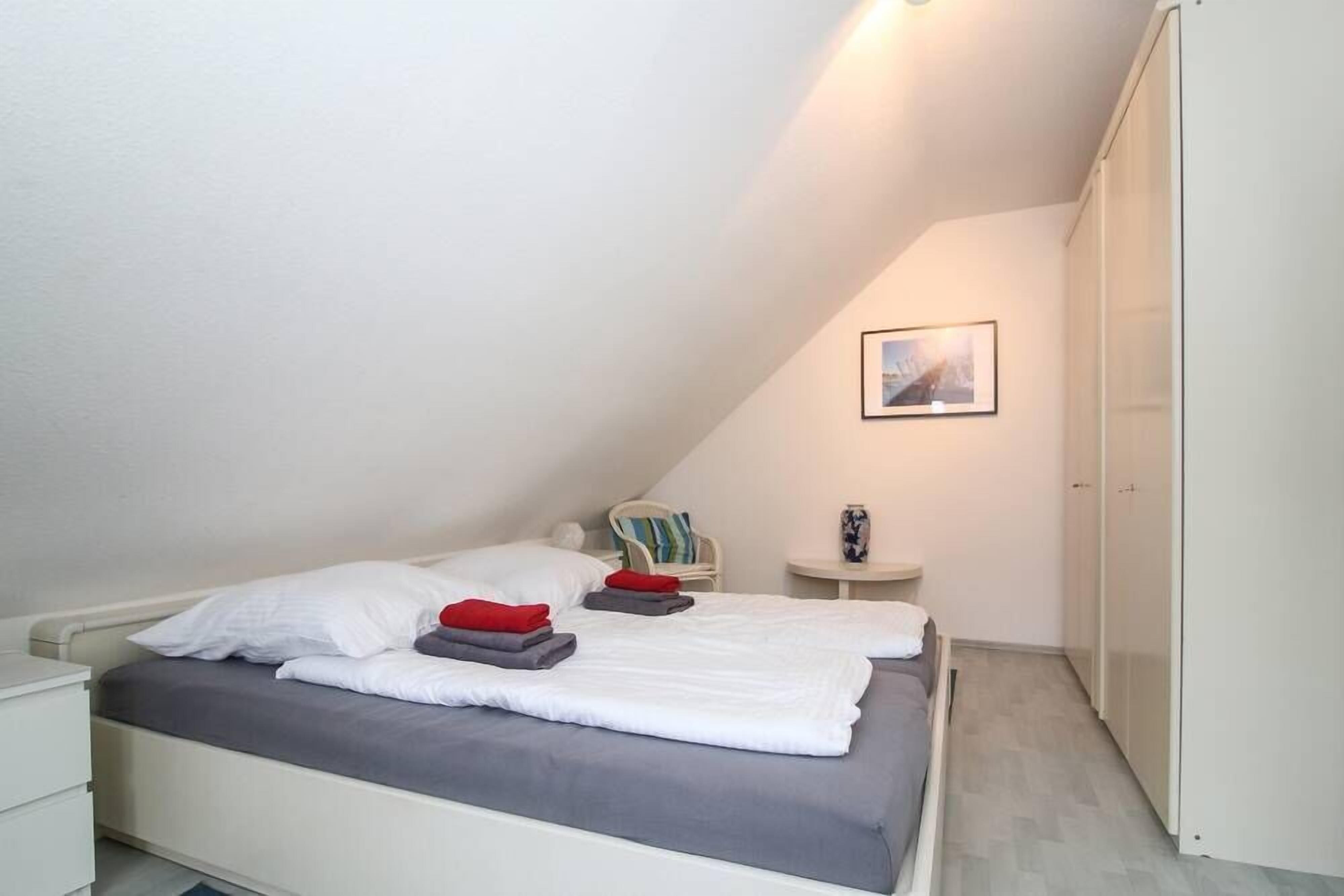 Un dormitorio con cama, una silla, una mesita y un armario.