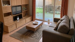 Una sala de estar con televisor, armarios de madera, sofá y puerta corrediza al exterior.