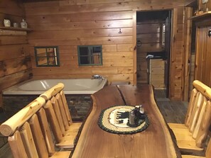 Ein Holzblockhaus-Innenraum mit einer großen Badewanne, Holzstühlen und einem Esstisch.