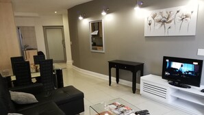 A modern living room with a black sofa, a glass coffee table, and a flat-screen TV. - Luxury, comfortable and secure home away from home for the best JHB experience (Sandton)