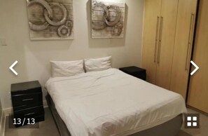 A bedroom with a bed, two nightstands, a wardrobe, and wall art.