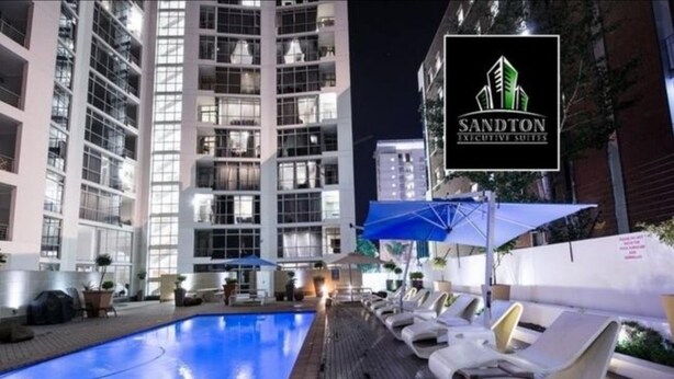 A poolside area with lounge chairs and a sign for Sandton Executive Suites. - Luxury, comfortable and secure home away from home for the best JHB experience (Sandton)