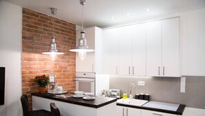 Una cocina compacta con armarios blancos, una pared de ladrillo decorativa, dos lámparas colgantes y una pequeña isla con taburetes de bar.