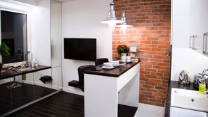 Una cocina moderna con una pared de ladrillo decorativa, un televisor de pantalla plana y una zona de comedor con una mesa de vidrio.