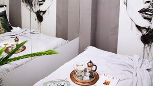 Una habitación moderna con un espejo grande que refleja un retrato blanco y negro, una cama bien hecha con una bandeja de té, y letreros con mensajes motivacionales.