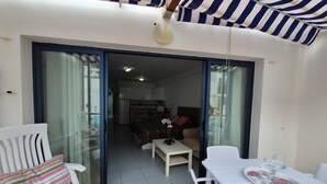 A room with a sliding glass door leading to a kitchen and living area, white furniture, and a striped awning. - Studio Playa Mogan Hungarian (Mogan)