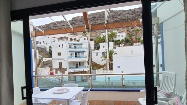 A balcony with a table and chairs, a pool in the background, and buildings with balconies. - Studio Playa Mogan Hungarian (Mogan)