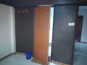 A room with a partially open door, a blue bucket, and a tiled floor. - Stansted Annex Hotel (Meru)