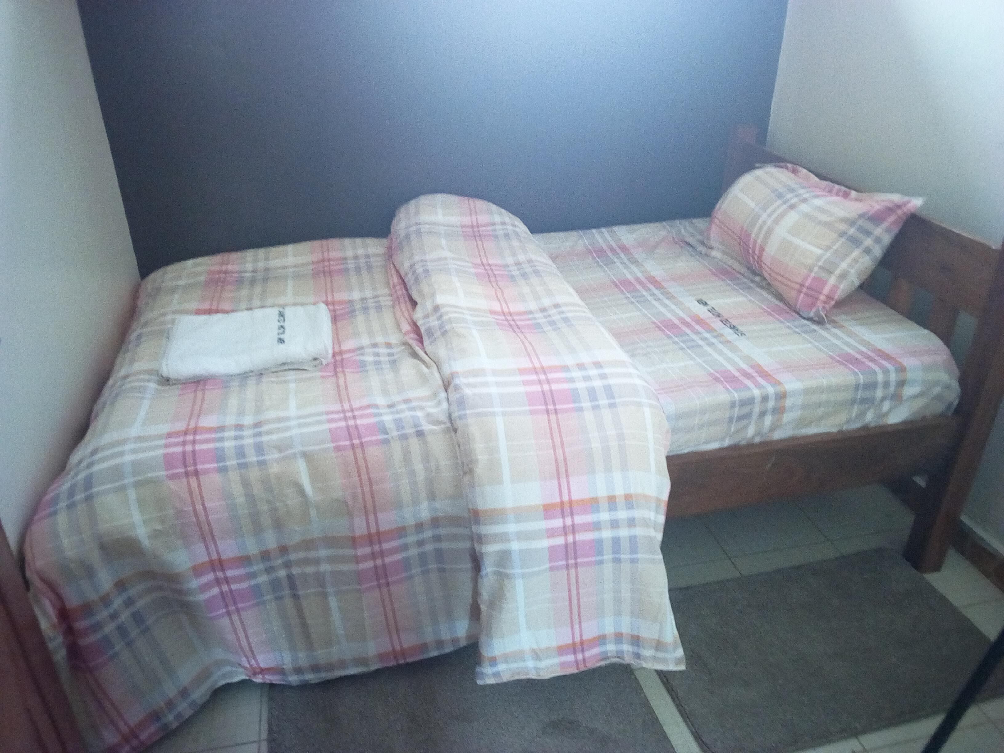 A small bed with a plaid bedspread and a pillow, a wooden headboard, and a small white towel on the bed.