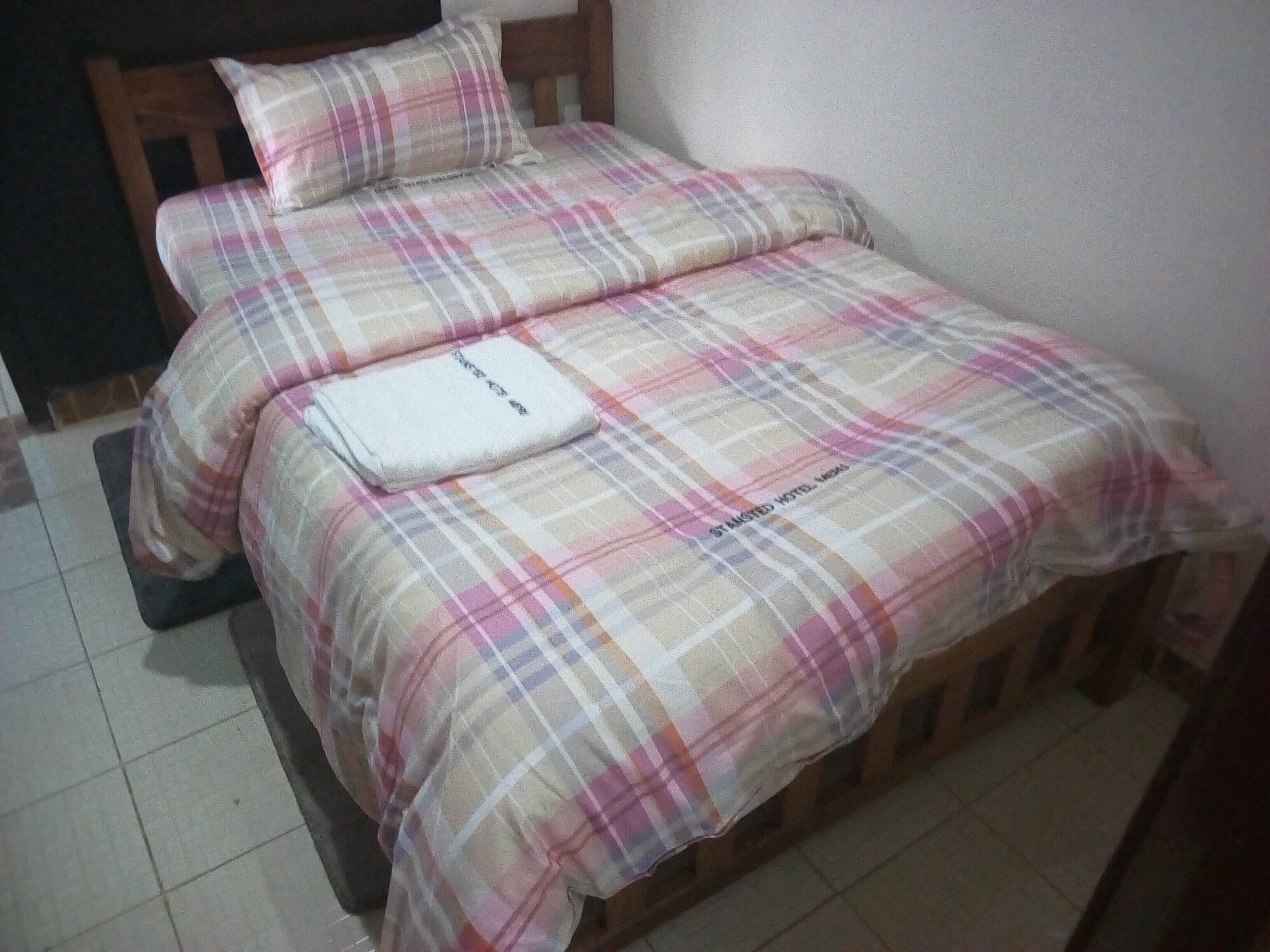 A bed with a plaid bedspread and pillows, a wooden headboard, and a small white pillow with text on it.