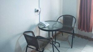 A small room with a television mounted on the wall, a table with two chairs, and a window with curtains. - Stansted Annex Hotel (Meru)