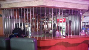 Un espace bar comprenant un comptoir, des tabourets de bar et des étagères remplies de bouteilles.