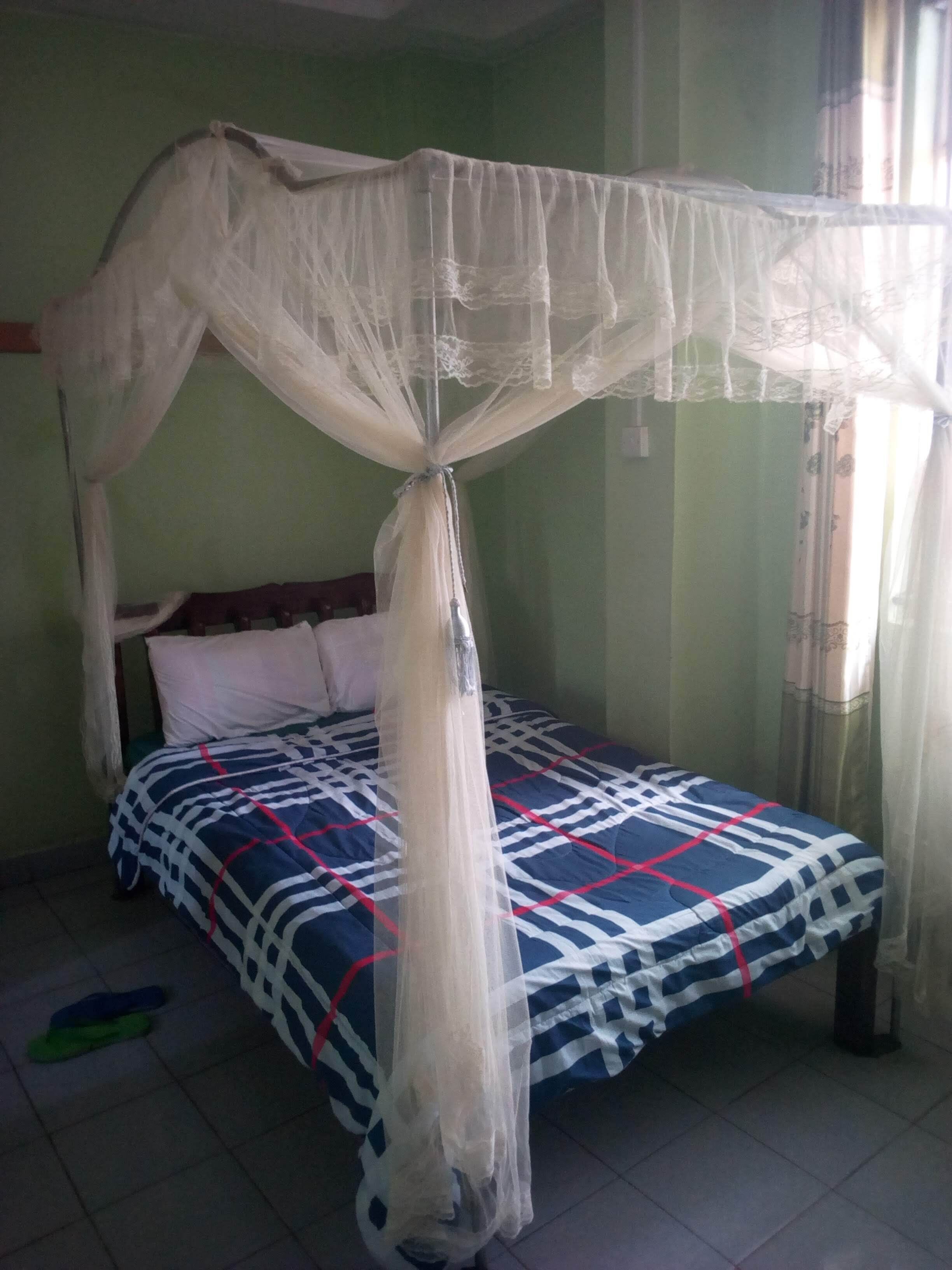 Un lit à baldaquin, une couvre-lit à motifs et une paire de pantoufles posées sur le sol.