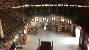 A rustic dining area with wooden tables and chairs, stone walls, and a thatched roof. - Manga Lodge (Andavadoaka)