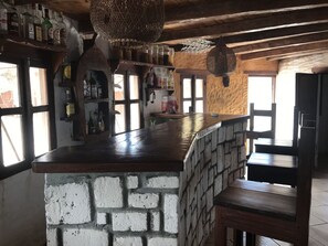 A rustic bar area with a stone counter, wooden shelves with liquor bottles, and hanging light fixtures. - Manga Lodge (Andavadoaka)