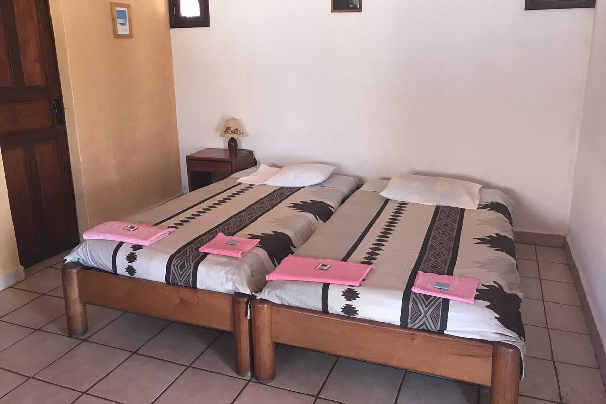 A double bed with patterned bedding, a wooden headboard, a small bedside table with a lamp, and a door.