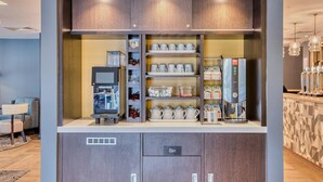 Une petite cuisine équipée d’une machine à café, de distributeurs de thé et de café, et de placards de rangement.