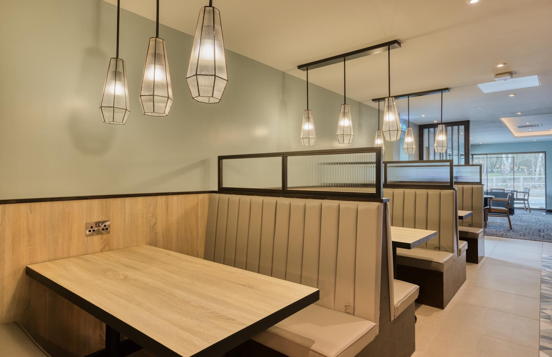 A restaurant interior with wooden tables, cushioned booths, and pendant lighting.