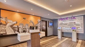 Un espace d’accueil d’hôtel au design moderne, comprenant un comptoir d’accueil, un écran numérique et un mur orné de phrases inspirantes.