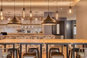 A bar area with multiple stools, a counter with taps, and pendant lighting. - Premier Inn Uckfield (Uckfield)