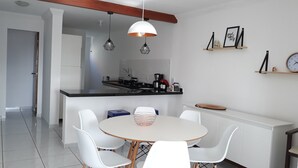A modern kitchen with a central island, white chairs, pendant lighting, and a white cabinet. - APARTMENT ON THE BEACH (Bessa)