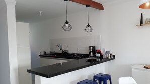 A modern kitchen with a black countertop, white cabinets, and two blue bar stools. - APARTMENT ON THE BEACH (Bessa)