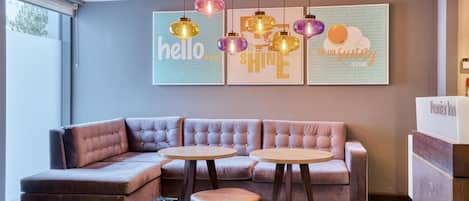 A modern hotel room with a sectional sofa, two round tables, and a decorative ceiling light fixture.