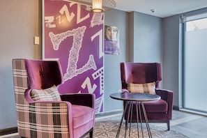 Una habitación con dos sillones cómodos, una mesita redonda y una pared decorativa con diseños abstractos.