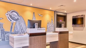 Un comptoir d’accueil d’hôtel orné d’une fresque représentant un paysage urbain, un ordinateur Dell et une enseigne Premier Inn.