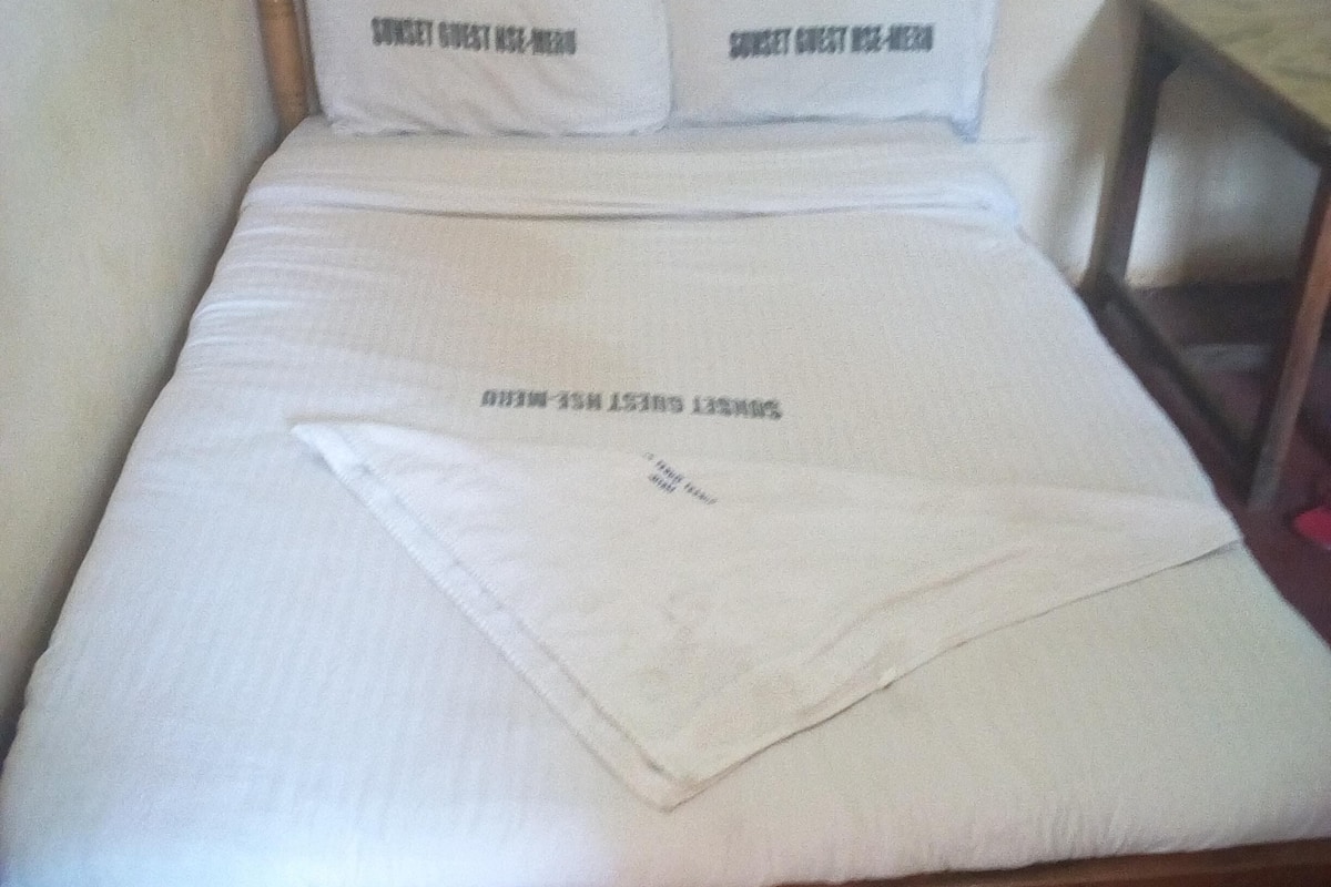 Una cama con estructura de madera, ropa de cama blanca y dos almohadas con texto.