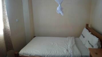 A single bed with a wooden frame, white bedding, and a mosquito net hanging above.