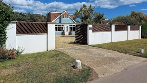 A house with a gated driveway, a sloped lawn, and a clear blue sky. - 5 bedroom accommodation in Elmer, near Bognor Regis (Elmer, near Bognor Regis)