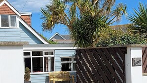 A house with a blue exterior, a wooden fence, a bench, and a palm tree. - 5 bedroom accommodation in Elmer, near Bognor Regis (Elmer, near Bognor Regis)