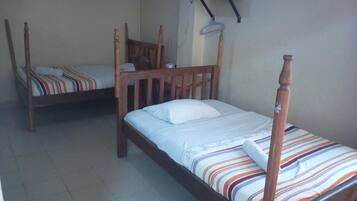A room with two wooden beds, one with a striped bedspread and the other with a plain one.
