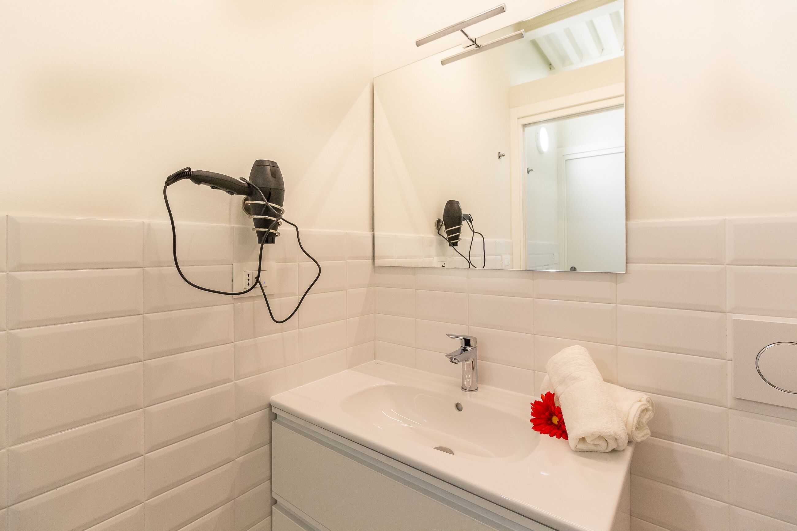 A bathroom with a white sink, a mirror, and two hair dryers mounted on the wall.
