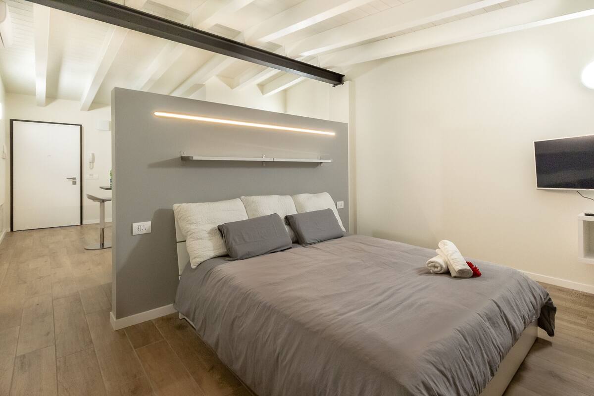 A modern bedroom with a large bed, a mounted TV, and a built-in shelf above the bed.