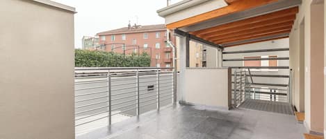 Un espacio al aire libre cubierto con barandilla de metal, suelo de baldosas y una escalera que sube a un nivel superior.