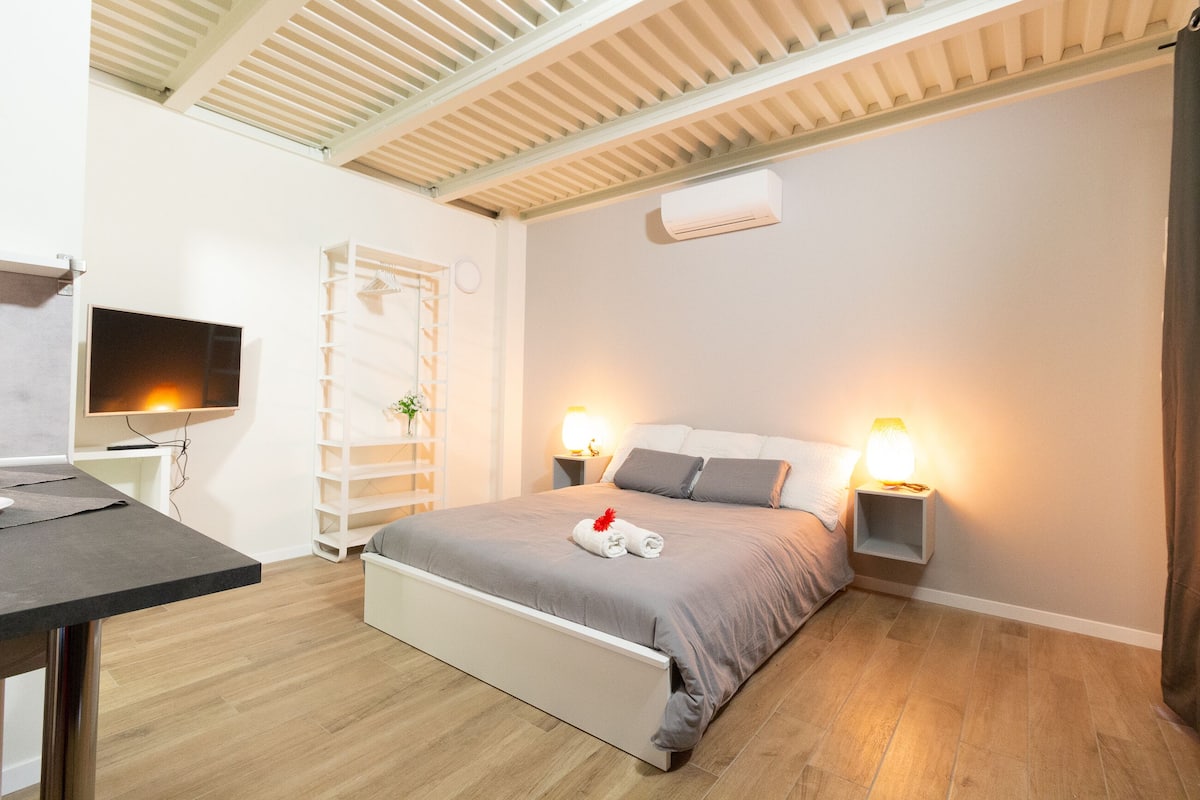A modern bedroom with a bed, bedside lamps, a TV, and a desk.