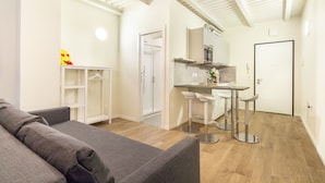 En moderne lejlighed med en grå sofa, et tekøkken, en glasvægsbruser og en hvid dør.